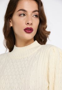 Pulover cu tricotaj în cablu de culoare crem, cu guler înalt ribat și model texturat. Material moale și cald, cu o siluetă ajustată.