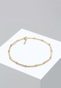 Collana in oro con delicati anelli e accenti testurizzati, dotata di chiusura a moschettone, esposta su un supporto geometrico bianco.