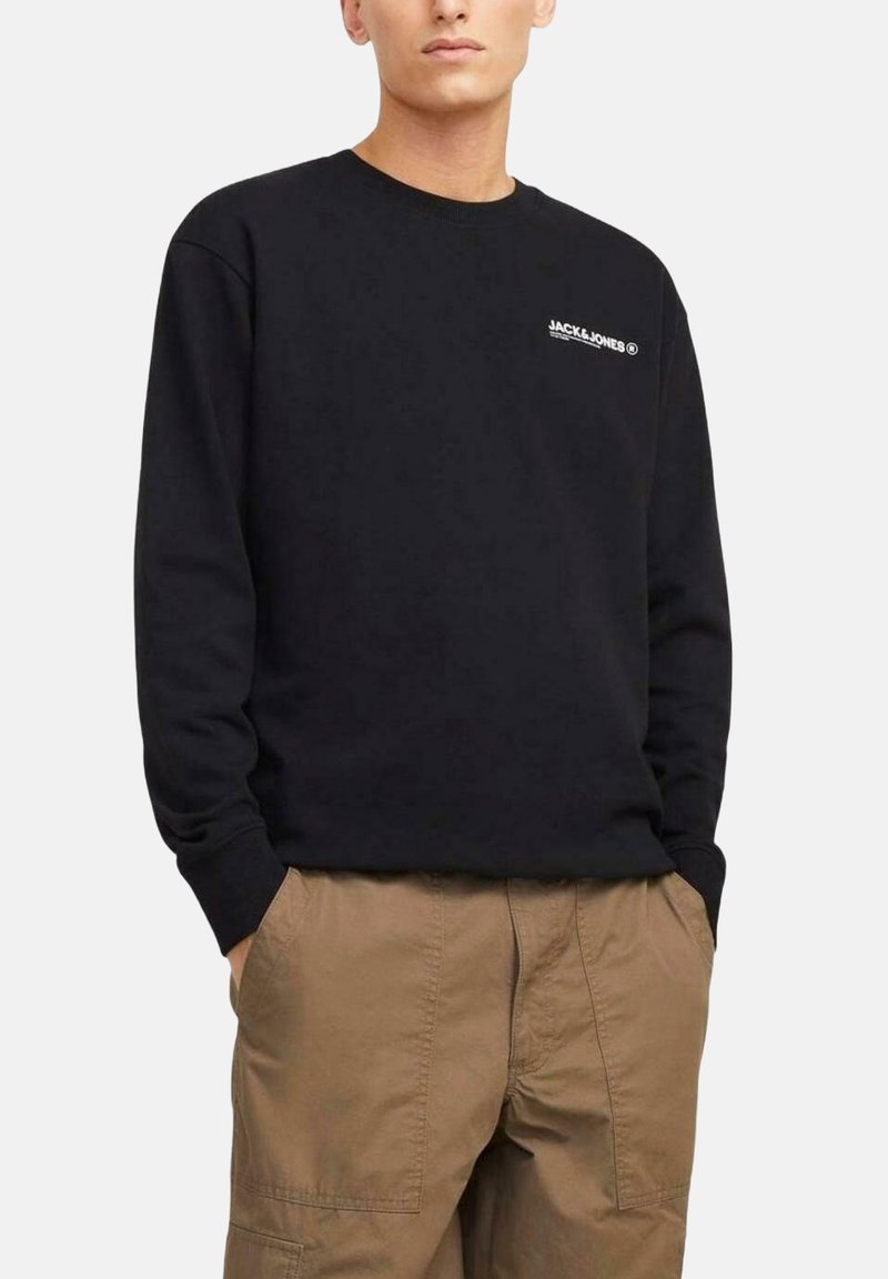 Sudadera negra de manga larga y cuello redondo, con un logotipo blanco en el lado izquierdo del pecho y un corte relajado. Combinada con pantalones cargo beige.