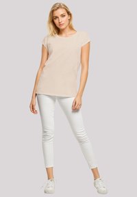 Light beige short-sleeve t-shirt with a round neck, paired with white fitted pants and white sneakers. Smooth texture, casual design.