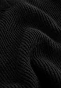 Tissu noir côtelé avec une texture douce, présentant des lignes en relief formant un motif ondulé. Le matériau semble chaud et dense.