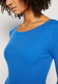Blue ribbed knit top featuring a wide neckline and fitted design, showcasing a smooth texture and vibrant color.