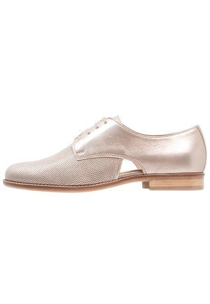 Chaussure Oxford en cuir beige clair avec bout perforé, découpe latérale, fermeture à lacets et talon bas en bois.