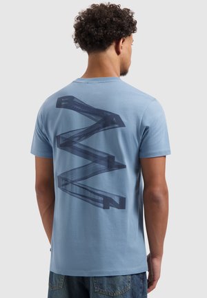 Lichtblauwe katoenen T-shirt met een grote marineblauwe zigzaggrafiek op de achterkant, korte mouwen en een ronde halsuitvoering.