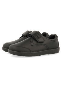 Calzado negro con un upper sintético suave, punta redondeada y correa de gancho y bucle. Cuenta con una suela texturizada para mayor agarre y un cuello acolchado.