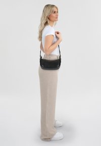 Zwarte leren schoudertas met een gladde afwerking, minimalistisch ontwerp en verstelbare schouderband, gedragen tegen een lichte outfit.