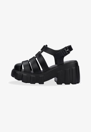 Black sandals with thick, chunky soles, featuring open-toe design and multiple horizontal straps. Adjustable ankle buckle for fit.