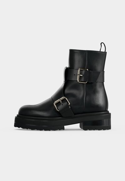 Bottine en cuir noir avec deux boucles argentées, semelle épaisse et languette à l'arrière.