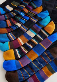 Calze assortite di diversi colori; principalmente scure con combinazioni di blu, arancione, viola e motivi a righe. Materiale morbido e varie trame.