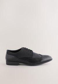 Chaussure habillée pour homme en cuir noir et tissu avec détails brogue et lacets, vue de profil sur fond uni.