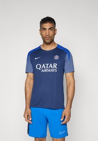 Marineblå Nike trøje med lyseblå accenter, "QATAR AIRWAYS" logo i hvid, parret med blå shorts. Glat, atletisk materiale.