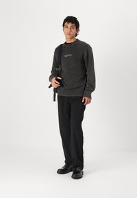 Mörkgrå stickad tröja med ribbade ärmslut och nederkant, med minimalistisch branding. Kombinerad med svarta byxor och glänsande svarta skor.