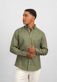 Olijfgroene, knoopsluiting shirt met lange mouwen en een borstzak. Bevat witte knopen en een subtiel logo op de zak.