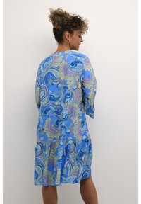 Mėlyna paisley suknelė su trim ketvirtadaliais rankovėmis, daugiapakopė struktūra, tekantis audinys, sudėtingi raštai žalių, geltonų ir rožinių atspalvių.