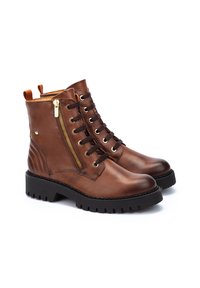 Bottines en cuir marron avec un bout rond, semelle en caoutchouc noir, laçage à l'avant, fermeture éclair sur le côté et tirette orange contrastante à l'arrière.