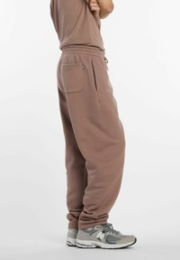 Pantalones de chándal marrones de corte holgado con cintura elástica, bolsillos laterales y tejido texturizado. Combinados con zapatillas deportivas grises.