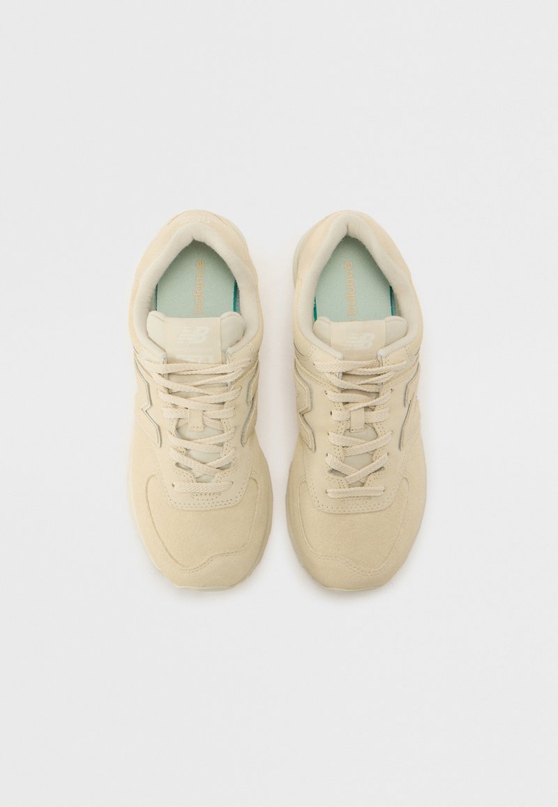 Zapatillas de gamuza beige con puntera redondeada, que presentan cordones planos y una suela de goma texturizada. Acento azul claro en la plantilla.