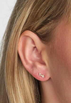 Uhan v zlatem tonu z ukrivljenim dizajnom, okrašen z majhnimi prozornimi dragimi kamni, na ozadju bližnjega posnetka ušesa s ravnimi lasmi.