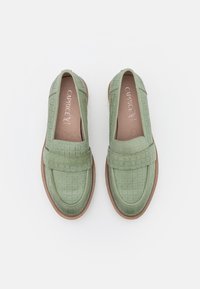 Mocassins en cuir synthétique vert avec un motif tissé texturé, dotés d'une semelle plate et d'un intérieur rembourré pour le confort.