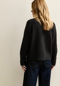 Czarny sweter z dzianiny z ribbowym dołem i mankietami, zestawiony z ciemnymi dżinsami. Posiada luźny krój i lekko skrócony fason.