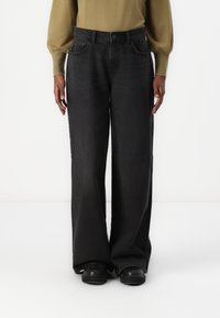 Jean en denim noir à jambes larges et taille haute, avec un design à cinq poches et un délavage subtil. Associé à un pull ajusté vert olive.