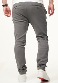 Gray sweatpants with a tapered fit, featuring two back pockets with button closures. Worn with white sneakers displaying red soles.