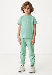 Mintgrünes Baumwoll-T-Shirt mit kurzen Ärmeln und Logo, kombiniert mit passenden Jogginghosen mit elastischen Bündchen und weißen Sneakers.