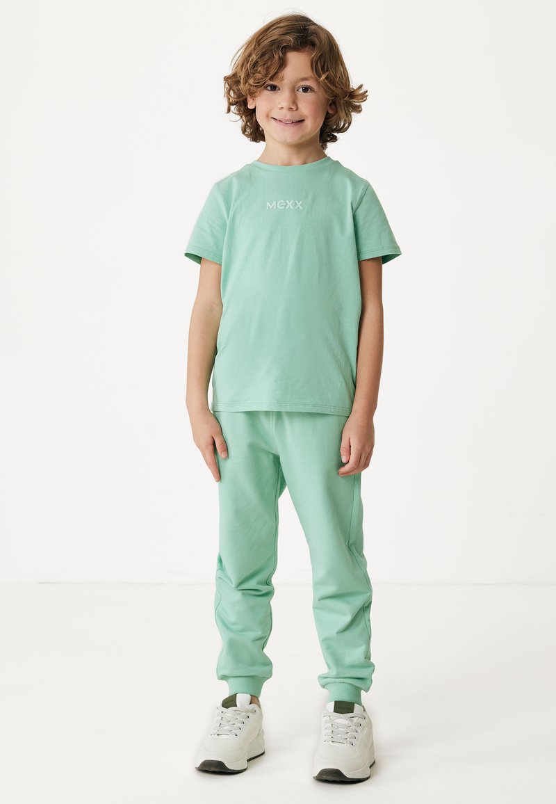 Mintgrünes Baumwoll-T-Shirt mit kurzen Ärmeln und Logo, kombiniert mit passenden Jogginghosen mit elastischen Bündchen und weißen Sneakers.