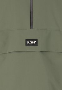 Olivgrön jacka med en slät, matt textur. Har en svart dragkedja och en rektangulär logotypapplikation märkt "SLOPE" på framsidan.