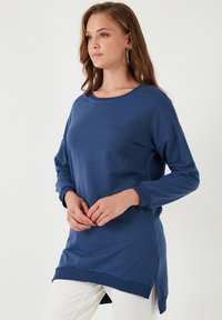 Námořnická modrá dlouhá halenka vyrobená z jemného materiálu, s kulatým výstřihem, postranními rozparky a volným střihem.