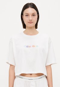 Hvit avkortet t-skjorte laget av bomull med korte ermer, med en flerfarget "Calvin Klein" logo på brystet.