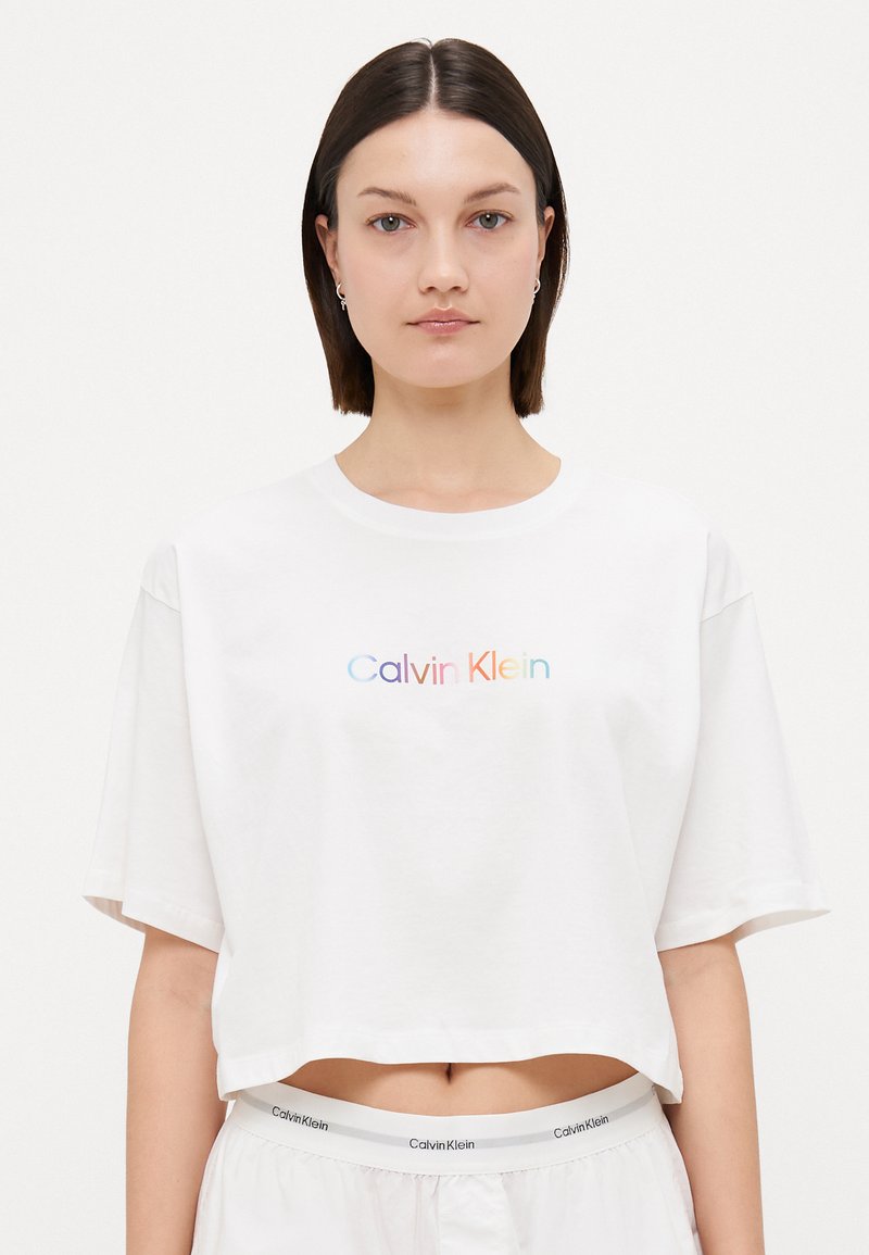 Hvit avkortet t-skjorte laget av bomull med korte ermer, med en flerfarget "Calvin Klein" logo på brystet.