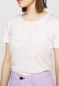 Triko s krátkým rukávem vyrobené z jemné, lehké látky, s růžovým a bílým tie-dye vzorem a kulatým výstřihem.