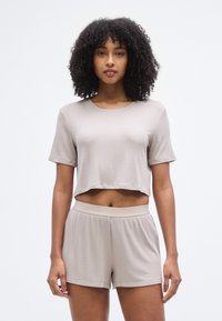 Ensemble composé d'un crop top beige et d'un short en tissu texturé, avec des manches courtes et une coupe décontractée, équipé d'une ceinture élastique sur le short.