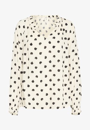 Blus med långa ärmar i krämfärgad tyg med svarta penseldragspunkter; har en V-ringning och samlade manschetter. Mjuk och genomskinlig textur.