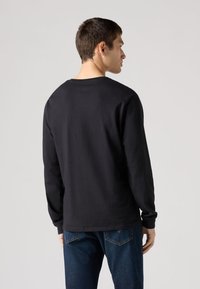 Černé tričko s dlouhým rukávem z bavlny, s kulatým výstřihem, volným střihem, hladkou texturou bez viditelných vzorů nebo akcentů.