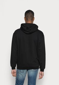 Sudadera negra con capucha de textura suave, con puños y dobladillo acanalados. Presenta un bolsillo tipo canguro y se combina con jeans de color azul claro.