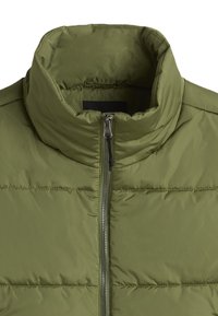 Olivově zelená prošívaná vesta s vysokým límcem, která má přední zip a horizontální prošívání přes hrudník pro texturu a design.