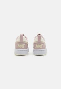 Baskets Nike rose et crème avec un tissu texturé, une forme arrondie, un col rembourré et une semelle blanche avec des éclats. Logo "NIKE" au niveau du talon.