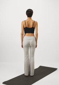 Svart avkortet topp, grå vide bukser med en teksturert finish, kombinert med en mørk yogamatte, sett fra bak. Enkel, minimalistisk design.