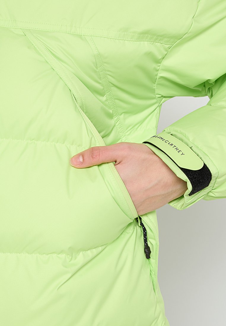 Giacca a vento verde chiaro con tasca con zip e polsino in velcro. Presenta una texture liscia e sezioni trapuntate per l'isolamento.