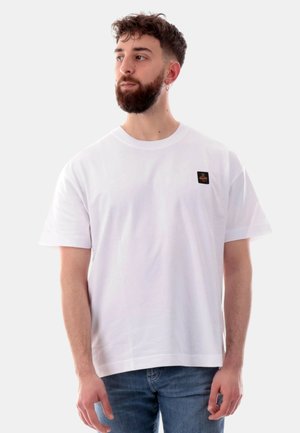 T-shirt bianco a maniche corte in cotone, con un piccolo logo quadrato nero sul petto. Vestibilità casual con scollatura rotonda.