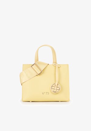 Petit sac à main en cuir jaune pâle avec poignées supérieures, large bandoulière réglable et charme rond doré suspendu à une poignée.