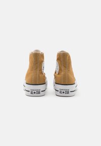 Pár hnědých vysokých tenisek Converse All Star zobrazených zezadu na bílém pozadí.