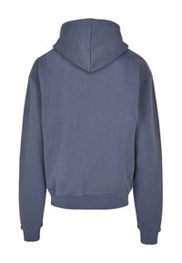 Mikina s kapucňou v vyblednutej modrej bavlne, s voľným strihom, rebrovanými manžetami a lemom, a textúrovaným povrchom. Zobrazený zadný pohľad.