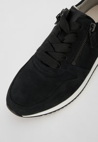 Baskets en suède noir avec un dessus texturé, bout arrondi, lacets plats noirs, détail de zip sur le côté et semelle en caoutchouc blanche.