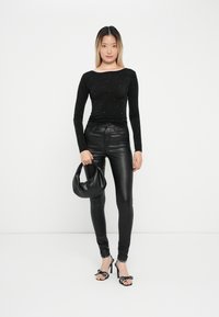 Zwarte lange mouwen top met verspreide versieringen, gecombineerd met strakke zwarte leren broeken en een zwarte hobo tas. Schoenen hebben stippenaccenten.