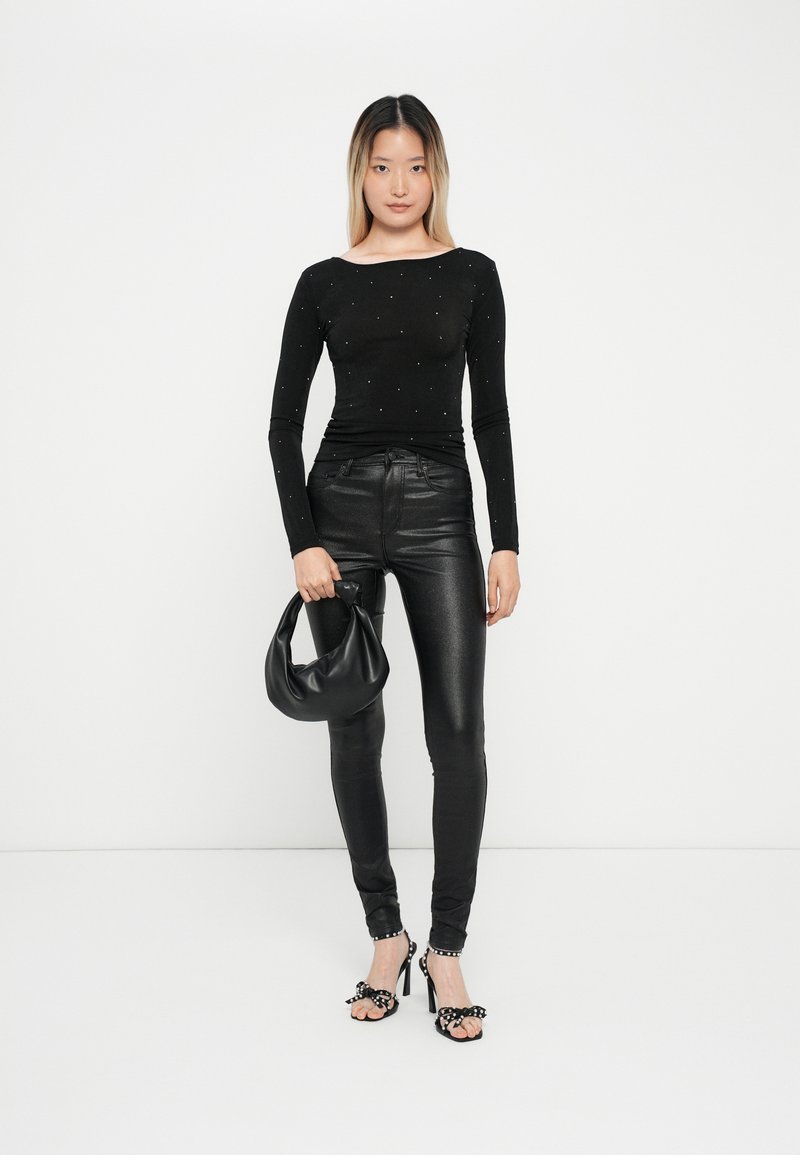 Zwarte lange mouwen top met verspreide versieringen, gecombineerd met strakke zwarte leren broeken en een zwarte hobo tas. Schoenen hebben stippenaccenten.