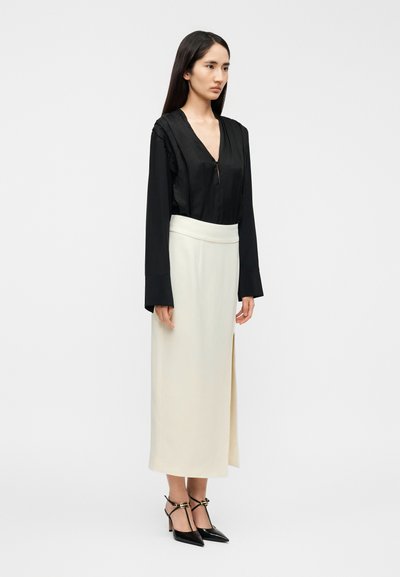 Μαύρο σατέν μπλουζάκι με μακριά μανίκια και βαθύ V-λαιμόκοψη, συνδυασμένο με λευκή, μήκους έως τον αστράγαλο φούστα με πλαϊνή σχισμή και εφαρμοστή μέση.