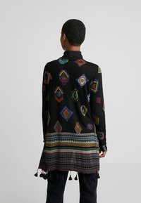 Schwarze Strickjacke mit bunten geometrischen Mustern, langem Design und dekorativen Quasten am Saum. Weicher Stoff, leichtes Material.
